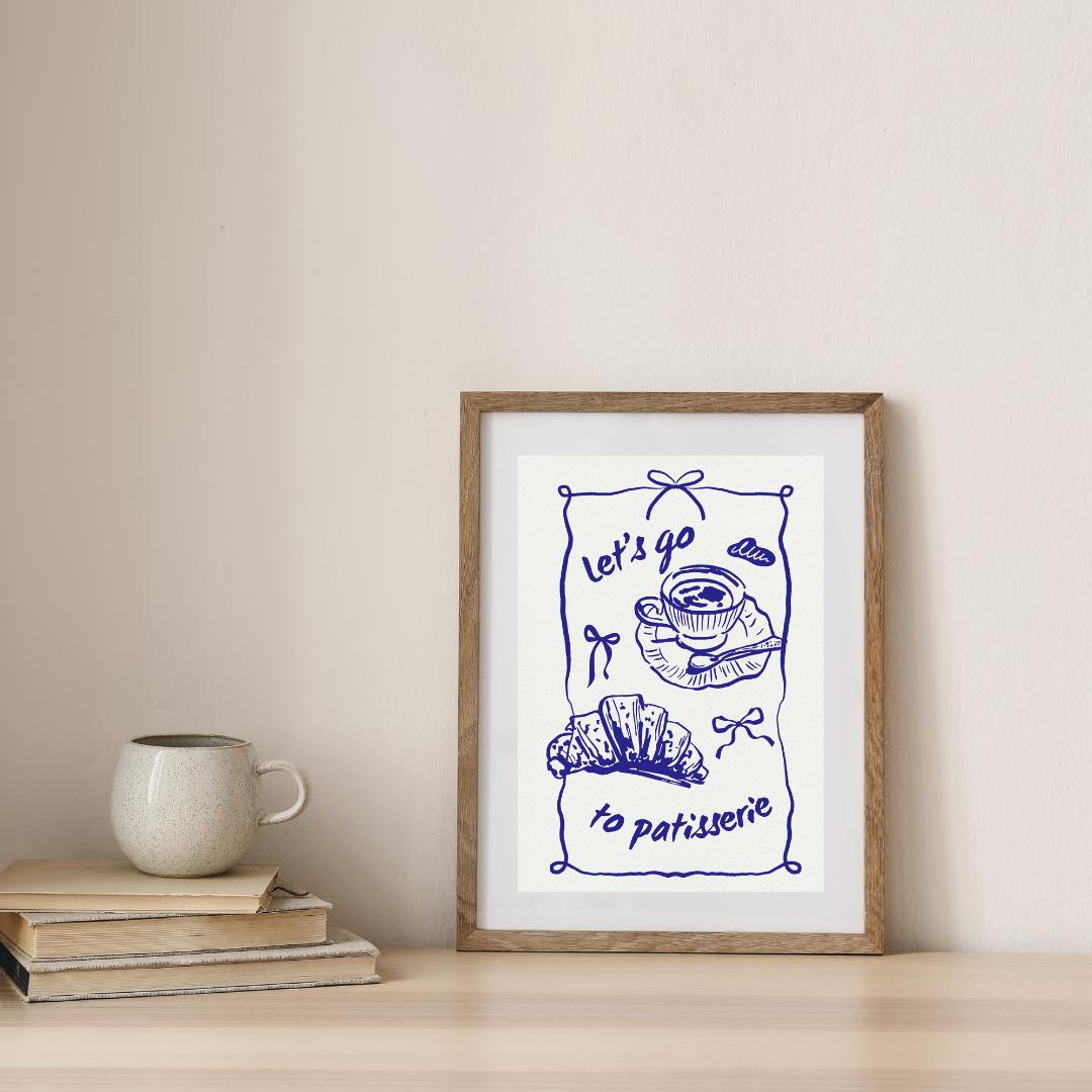 Framed artwork with 'Let's go to patisserie' text and illustrations on a wall above books and a mug.