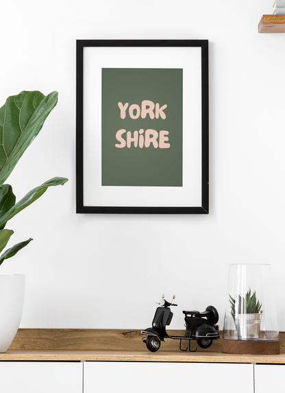 Framed artwork with 'York Shire' text on a wall above a wooden shelf.