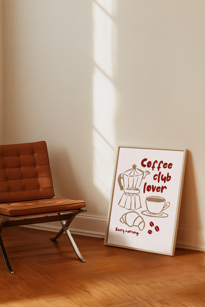 Framed artwork with 'Coffee club lover' text and coffee-themed illustrations on a wall next to a brown chair.